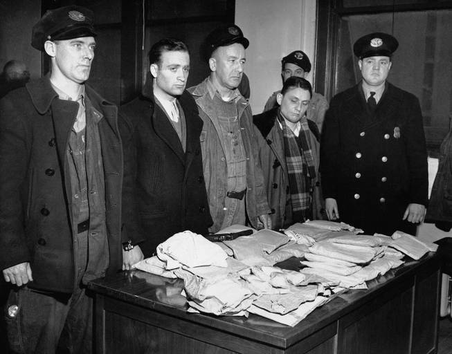 In this March 17, 1947 file photo, about 459 ounces of pure heroin valued at over one million dollars in the black market lies on table in Customs Enforcement Bureau in New York following seizure aboard the French freighter Saint Tropez after its arrival in New York City from Marseilles. Cesar Negro, Marseilles seaman, second from left, was arrested on charges of smuggling narcotics and Rene Bruchard, second from right, the ship's linen keeper, is being held for questioning. Port Patrol Officers Michael F. Munro, left; Arthur H. Cumming, center, and Lawrence F. Murray, right, are credited with discovering the heroin during a routine check of the seamen. 