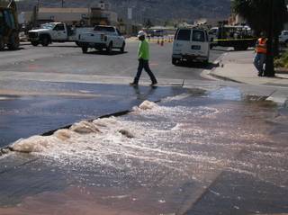 A worker walks past a water main break that closed Water Street in downtown Henderson on Tuesday.
