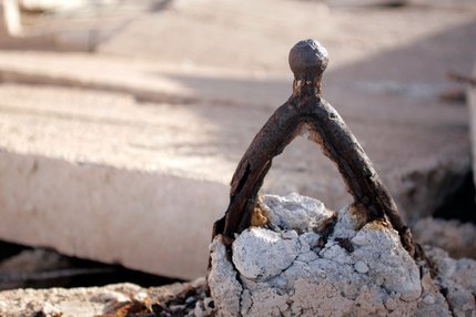 The lower control arm of an old Model T automobile, which was used to reinforce concrete, is now exposed as the wall of an old auto garage crumbles.