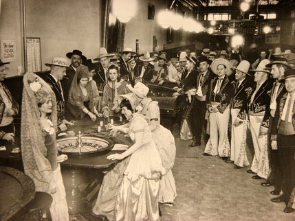 The Boulder Club beckoned its guests to enjoy the Old West. Here, men dressed in Mexican charro suits look on as western maidens play a game of roulette. Craps is being played at the next table.