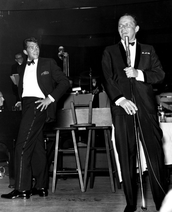 Dean Martin looks on as Frank Sinatra sings a number ...