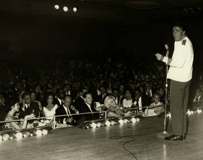 Peter Lawford performs at the Copa Room in the Sands Hotel during the 1960s.  Seated in the front rows of the star-studded audience are fellow Rat Pack members Sammy Davis Jr. and Dean Martin, actor Milton Bearle, actresses Marilyn Monroe and Elizabeth Taylor, and singer Eddie Fisher.