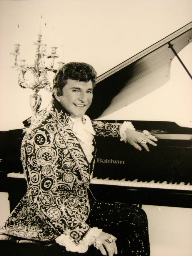 Liberace poses in front of a grand piano for a promotional photo advertising one of his numerous performances. His collection of rare and antique pianos, sequined bejeweled costumes, and countless items of memorabilia can be seen in the Liberace Museum in Las Vegas.