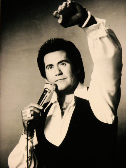 Wayne Newton brandishes a microphone and raises his fist in this promotional shot. Wayne Newton Boulevard was named in his honor.