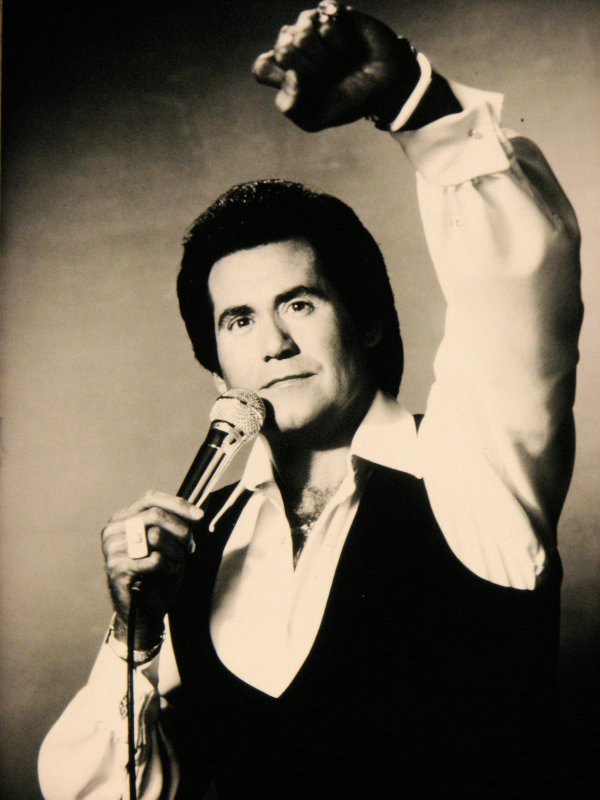 Wayne Newton brandishes a microphone and raises his fist in ...