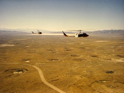 Air Force helicopters fly DOE radiation monitoring personnel over Yucca Flat during tests, in this now unclassified photograph.  Yucca Flat, where most nuclear weapons tests are conducted, is dotted with more than 200 subsidence craters from underground explosions.