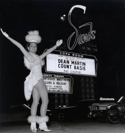 A Copa Girl poses in front of a Sands Hotel marquee advertising Dean Martin and Count Basie.
