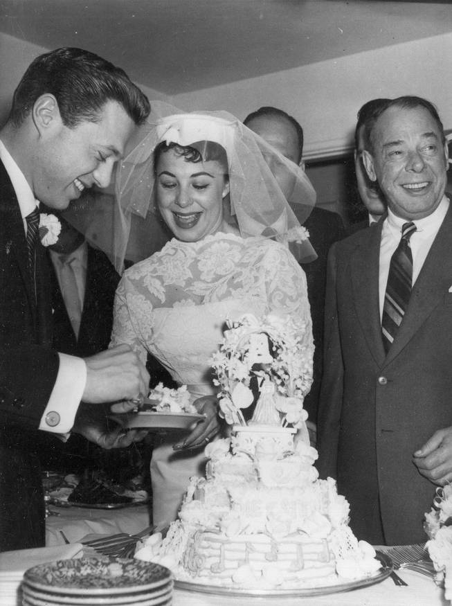 Comedian Joe E. Lewis looks on while singers Eydie Gorme and Steve Lawrence cut the first slice of their wedding cake at the home of El Rancho Vegas Hotel owner Beldon Katleman during their Dec. 29, 1957, wedding. 