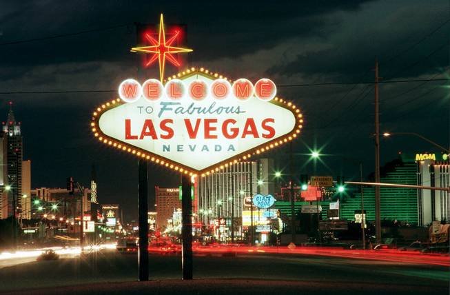Cars zoom by the sign welcoming motorists to Las Vegas on Nov. 13, 1997.  The sign's distinct shape and relatively small stature, 25 feet tall, set it apart from the other signs crammed along the Las Vegas Strip. Seven silver dollars back the seven letters of the word "Welcome" in affirmation of Nevada's nickname the "Silver State." 