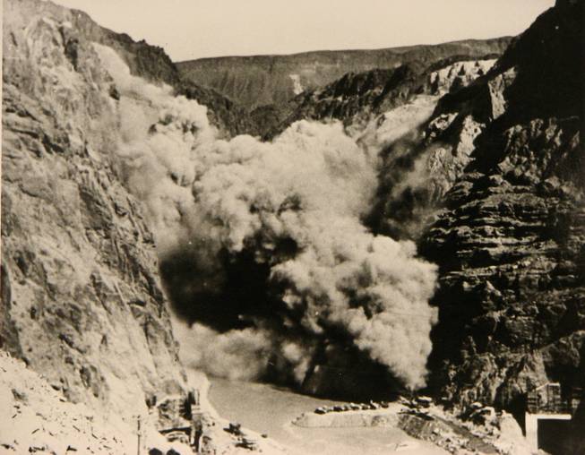 An explosion occurs during the construction of the Hoover Dam. Workers, called high-scalers, are suspended from the Black Canyon wall and would drill holes into the rock with 44-pound jackhammer drills. The holes are then loaded with dynamite in order to clear Black Canyon down to bedrock.
