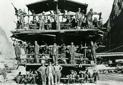 Workers smile for the camera in this picture showing a truck-mounted drill. The drill is used in the upper portion of the diversion tunnels. The diversion tunnels redirect the Colorado River around the construction site. Four tunnels are drilled, two on the Nevada side and two on the Arizona side. All are 56 feet in diameter and have been sealed since construction completed.