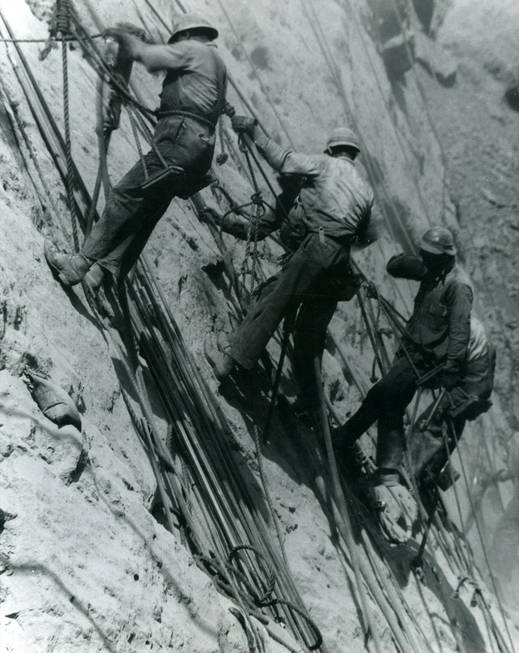 In April 1933, high scalers work to drill holes that ...