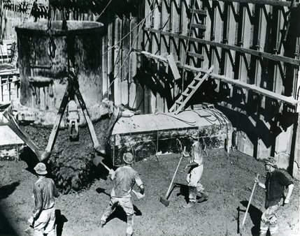 A gang of puddlers pack wet concrete into the base of Hoover Dam as an eight cubic-yard bucket spews out 16 tons of concrete at a time. The dam is a concrete gravity-arch which is designed to resist overturning, sliding and crushing at the toe. It's mass inspires safety and stability upon first glance.