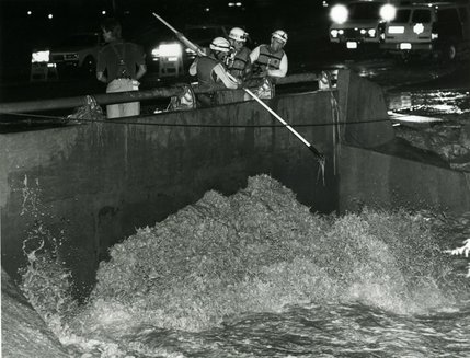 July 17, 1990.
Search and Rescue officers prod into flood waters to determine whether or not a vehicle is trapped against the bridge at Swenson Stteet. A 25-year old woman had drowned the previous day when flood waters swept her car into the the Flamingo Wash. Storms throughout July of 1990 caused $8.7 million in damage to infrastructure.