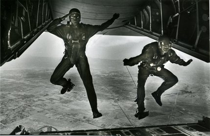 Airmen look before leaping out of a plane over the Nevada landscape. Nellis Air Force Base is named in 1950 after 1st Lt. William Harrell Nellis, a southern Nevada man who died in the Battle of the Bulge in 1944. Originally, the base consisted of a dirt runway, water well and small operational shack.