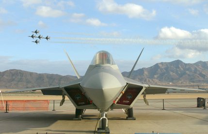 The latest generation of fighter technology, the F/A-22 Raptor, sits on static display as the famous Thunderbird Air Squadron fly their Thunderbird Diamond over the runway during the 