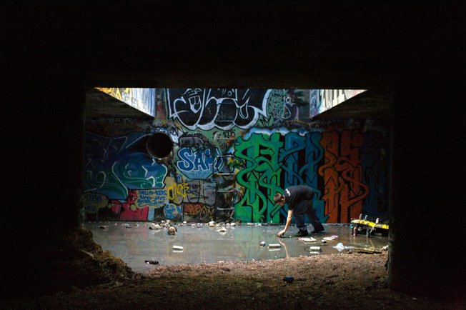 Graffiti artist Ruckoh reaches for a can of spray paint in a pool of water in a storm drain lit by a street grate almost directly under the Las Vegas Strip. 