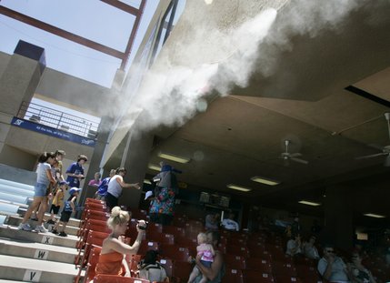 Team mascot Cosmo entertains fans and escapes the heat in the shade and under the misters of the grandstand during a rare day game at Cashman Field. 