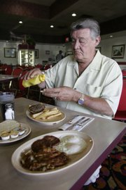 Klondike Sunset owner John Woodrum dresses up a 99-cent hamburger special Thursday.  
