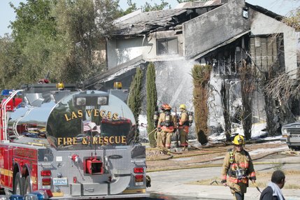 Firefighters spray fire retardant on a house after a twin-engine Piper Navajo crashed into a home on North Jones Boulevard near Cheyenne Avenue today.