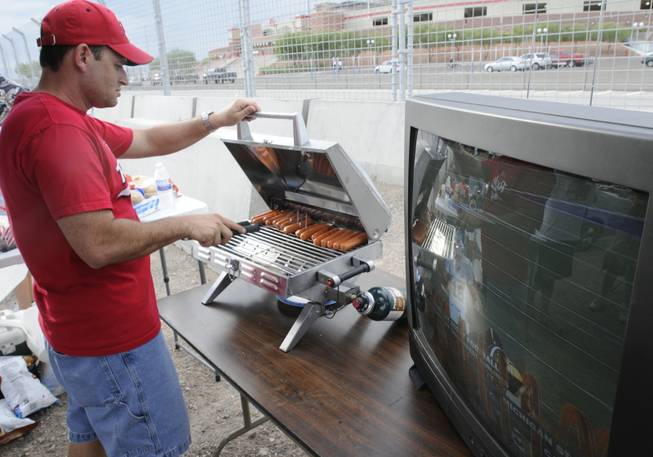 With the Michigan State vs. California game on a television close at hand, Eric Gallegos tends to some hot dogs on the grill while tailgating outside Sam Boyd Stadium.