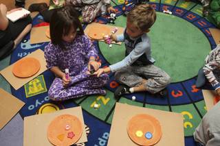 Triston Curtis, 6, right, shares a button with Rebecca Geissler, 6, while making pumpkin faces during the Boo! Boo! Halloween Pajama Party at Enterprise Library Oct. 27.