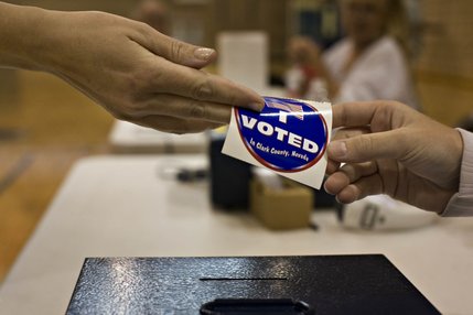 A volunteer gives a voter a sticker upon turning in their voter card at Bob Miller Middle School in Henderson