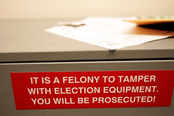 A sign warns people not to tamper with election equipment ...