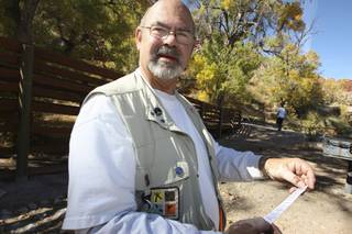 After finding a geocache hidden near the Calico Basin picnic area, John Sanderson, 64, reveals the log to be signed before returning the geocache to its original location during the Nevada Geocachers Association's hunt Saturday.