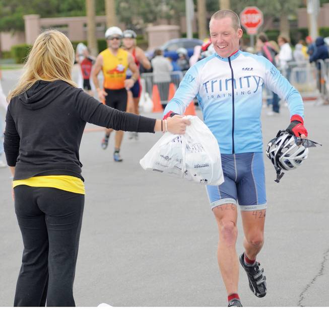 Silverman triathlete Glyn Learmonth is all smiles as he is handed a bag containing his running gear from a volunteer at the Henderson Multi-Gen Center after completing the swimming and biking stages of the race on Sunday.
