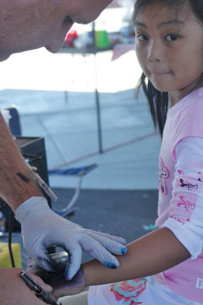 Nicole Lee, 7, waits in anticipation while temporary tattoo artist Frank Hawley puts the finishing touches on her tattoo. The booth was one of many at Goolsby Elementary School's Fall Festival.