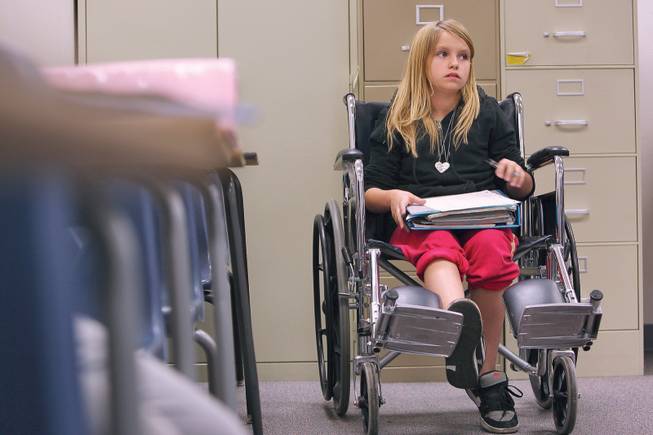 Abigale Houghton, 11, sits in a wheelchair while watching other students line up at her teacher's desk to turn in their papers during English class at Greenspun Junior High School.