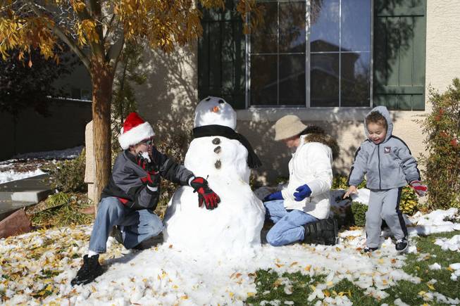 Nathan Day, 14, builds a snowman with his mom, Laura Price, and three-year-old brother, Aiden Price, while playing in the snow in front of their home in Anthem Thursday afternoon.
