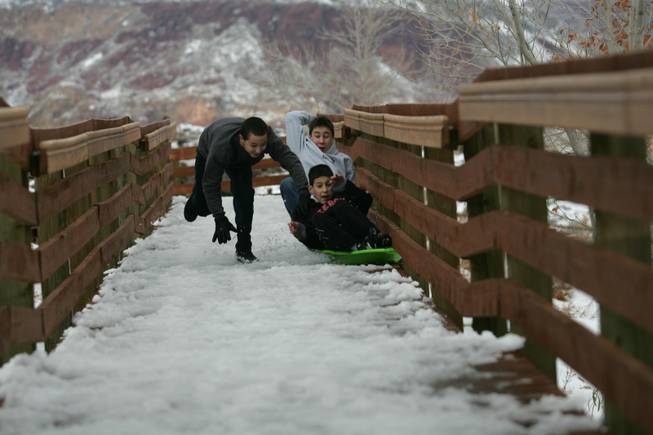 Benjamin Martin, 11, rides on a sled as he is pushed by Mark Kim, 15, left, and Tony McBeth, 17, while playing in the snow at Red Springs in Red Rock Canyon National Conservation Area Thursday.
