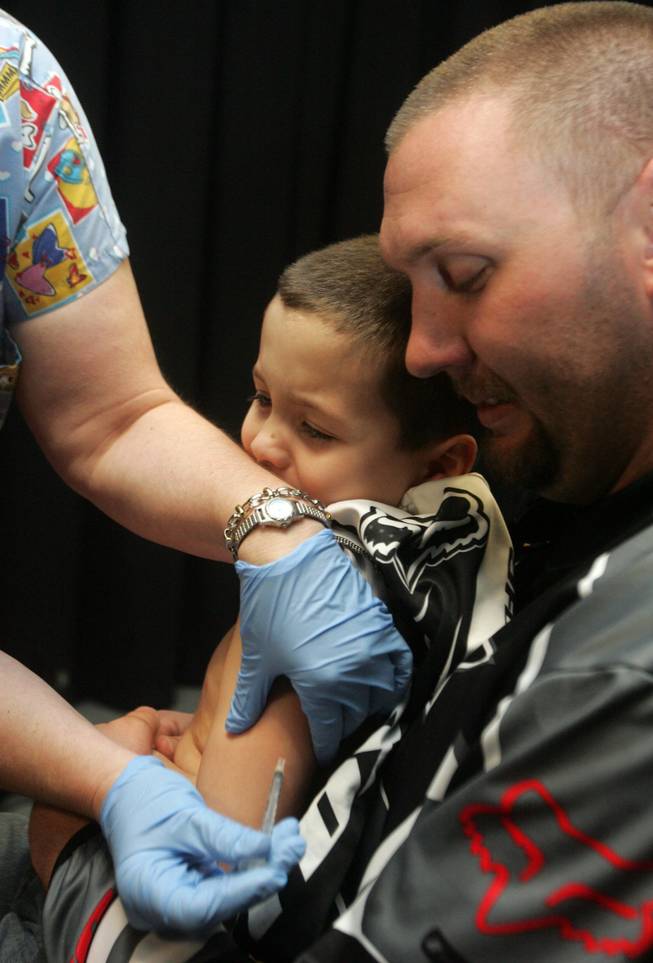 Dan Raymond, right, holds on tight to his stepson, Trennan Boone, center, as registered nurse Donna Hines, the health center coordinator, left, gives Boone an immunization during the community health fair at C.T. Sewell Elementary School Friday.