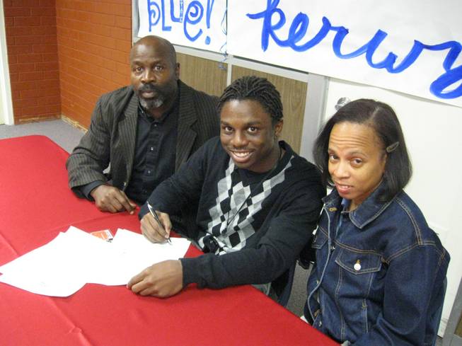 Kerwynn Williams, in between parents Kendall and Ingrid Williams, prepares to sign an offer to play at Utah State next fall.