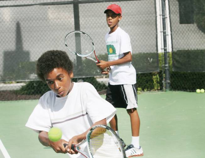 Henderson tennis player Yannik Mahlangu, 12, returns a ball as brother Nicholas, 16, looks on during practice at the ClubSport Green Valley.