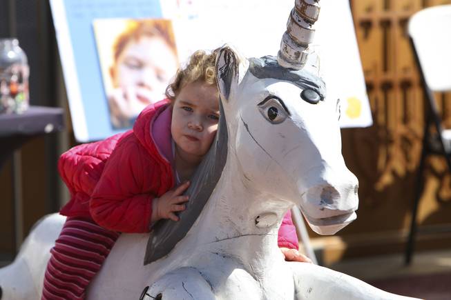 Two-year-old Addison Zaricki relaxes on a toy unicorn in the playground area while listening to Magician Mac King read during storytime Wednesday in Town Square plaza in celebration of National Reading Month.