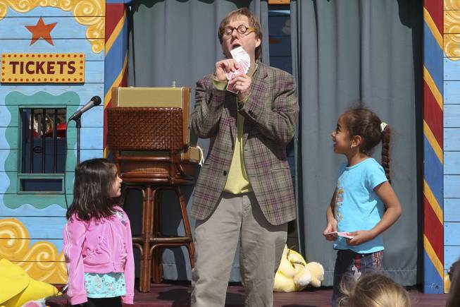 Lily Isho, 4, and Brianna Milena, 5, right, assist Magician Mac King perform a card trick during storytime Wednesday in Town Square plaza in celebration of National Reading Month.