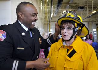 North Las Vegas city councilwoman Stephanie Smith, right, dons a fire protection suit with the help of Capt. Cedric Williams before the official first fire hose spraying at  North Las Vegas' newest fire station Thursday.