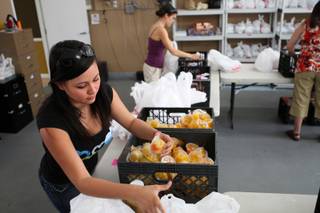 Jenny Monrroy places cups of peaches into sack lunches for students in need while volunteering Thursday with Acts of Kindness at the Caring 4 Kids warehouse in Henderson.