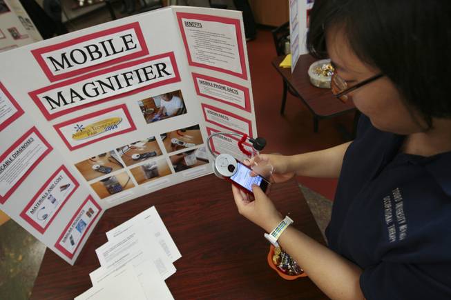 Melody Lee texts on a phone using a mobile magnifier while demonstrating her invention Thursday during the annual student Assistive Technology Fair at Touro University.