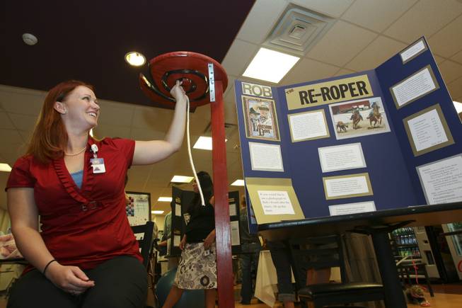 Sitting under her invention, McKinnon Carroll demonstrates how an injured rodeo roper can learn to rope with their left hand using her Re-Roper invention Thursday during the annual student Assistive Technology Fair at Touro University.