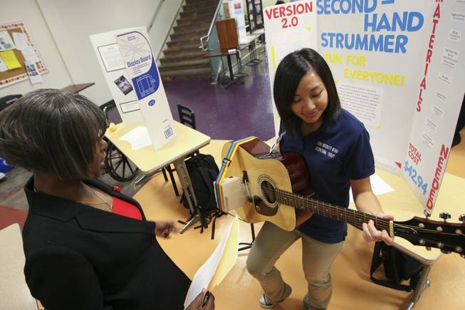 Administrative Assistant Althea Jones watches Maryann Gonzales, right, play the guitar with her motorized Second-hand Strummer invention Thursday during the annual student Assistive Technology Fair at Touro University.