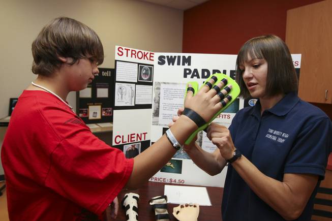 Irina Sobyanina fits her swim paddle invention onto the hand of Lawrence Morales, 14, while demonstrating how it works Thursday during the annual student Assistive Technology Fair at Touro University.