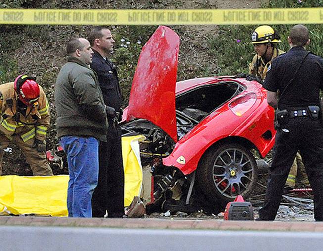 Investigators work on the front half of a red Ferrari that crashed into a light pole in Newport Beach, Calif.