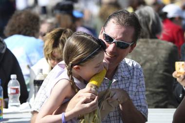 After waiting in a long line for a favorite treat, Camile Thevenut digs into an ear of grilled corn with her dad, Roy, during the annual Art in the Park event in Boulder City.