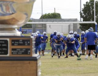 The Basic High varsity football squad practices as the Henderson Bowl trophy sits at the 50 yard-line on Monday afternoon.