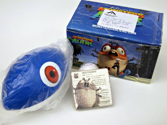52. Box from DreamWorks of stuff from Monsters vs Aliens. Included is a blue and white football with an eye on the front, a pack of nine cards with all the monsters' information and a white tennis-sized rubber ball that says "Intru 3D" in purple.