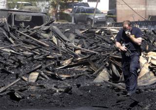 A Henderson Fire Department investigator holds a mask to his face Wednesday as he walks through rubble the day after a fire in a Henderson pallet yard near Boulder Highway and West Barrett Street.